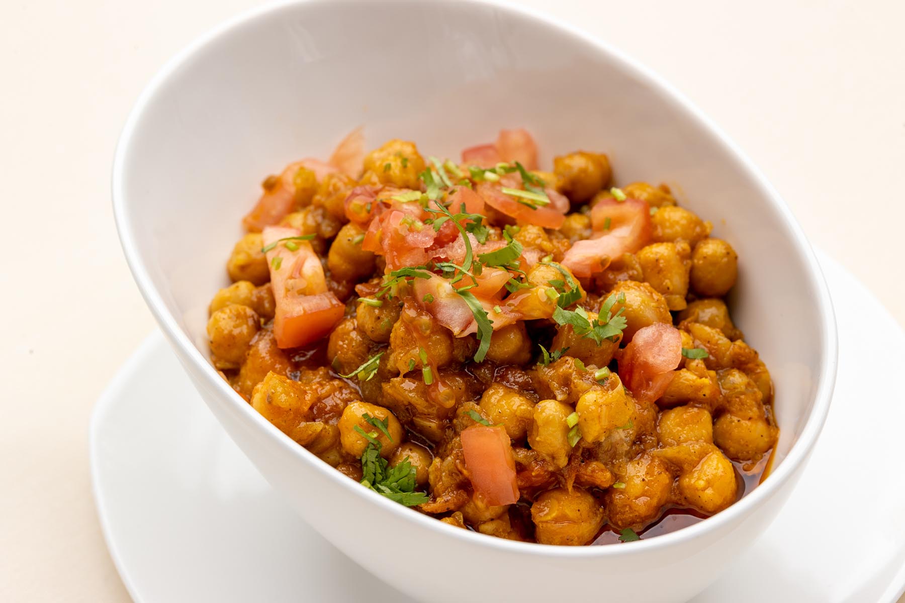 White bowl filled with spiced chickpea curry garnished with chopped tomatoes and cilantro.