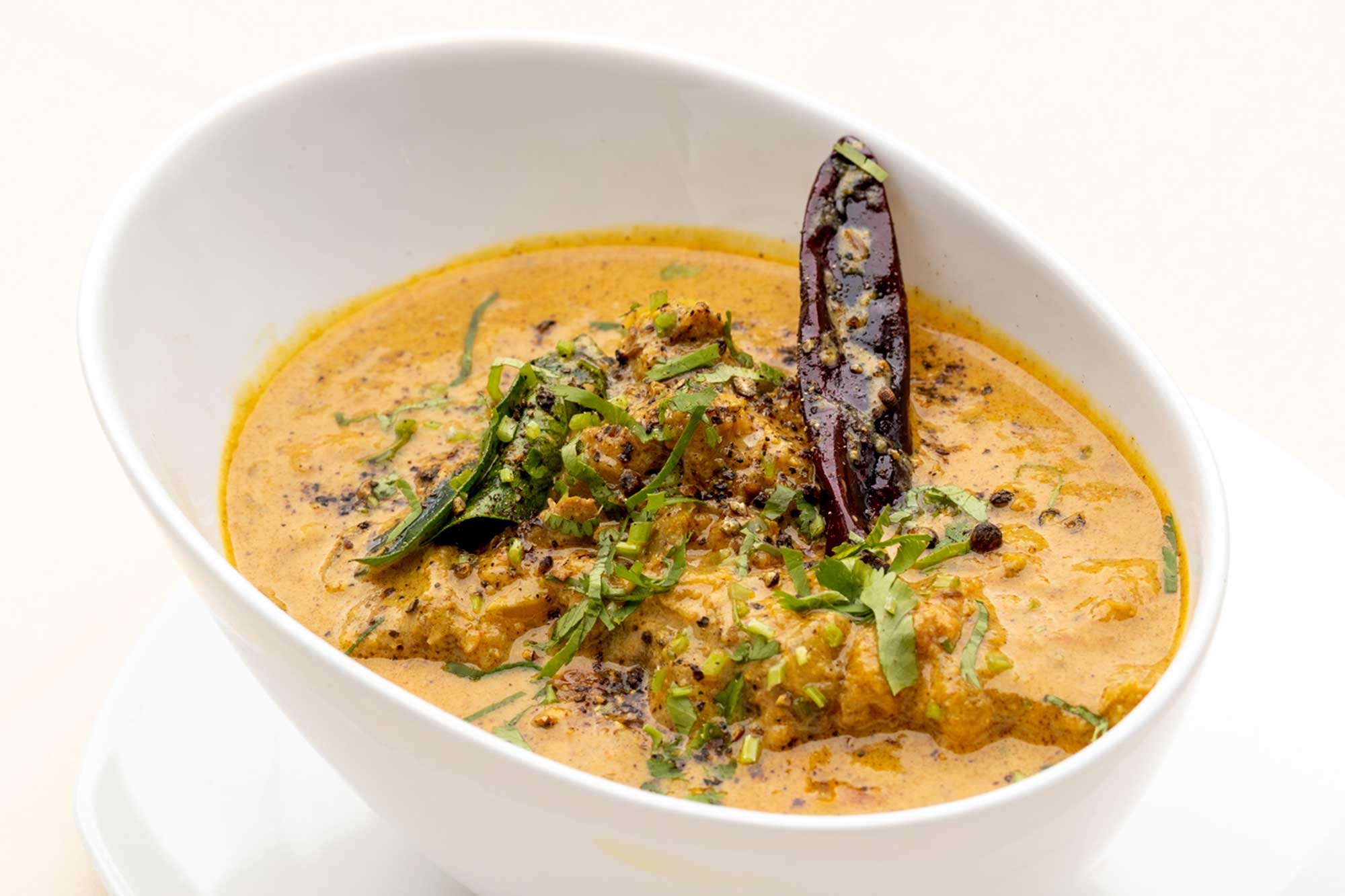 White bowl of Indian curry garnished with fresh herbs and whole dried red chili.