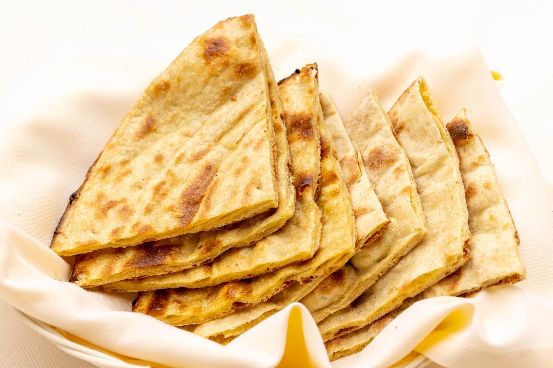 Stack of folded, toasted Indian flatbreads in a cloth-lined basket.