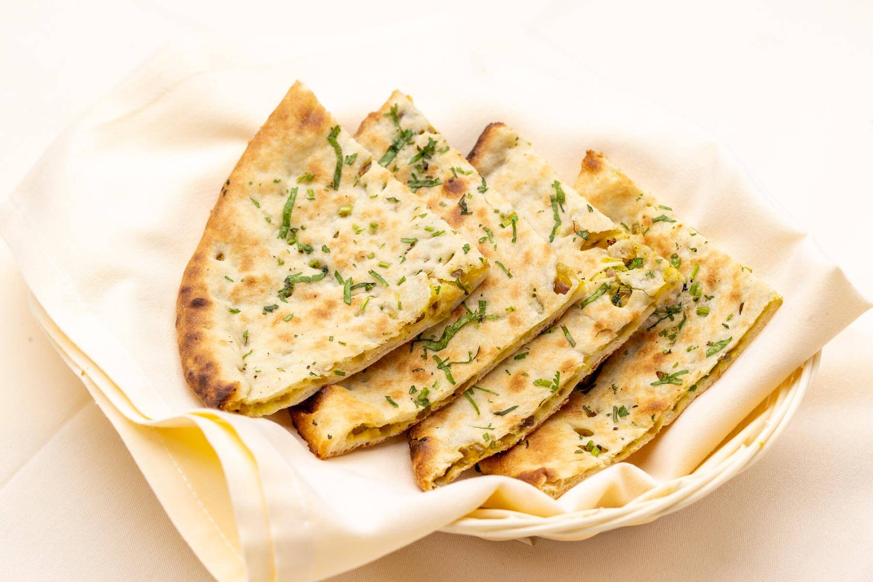 Basket of four pieces of garlic naan sprinkled with chopped herbs on a cloth napkin.