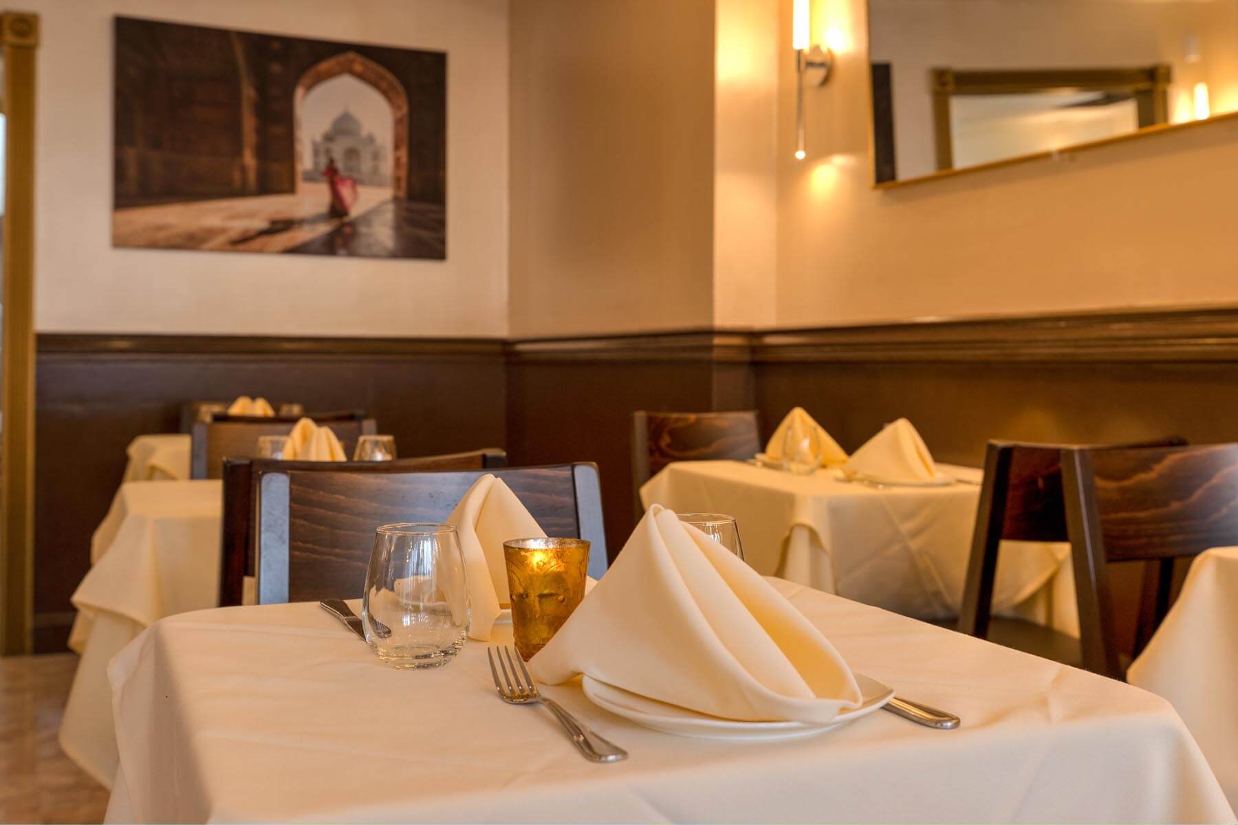 Cozy restaurant dining room with tables set with white tablecloths, folded napkins, glassware, and utensils.